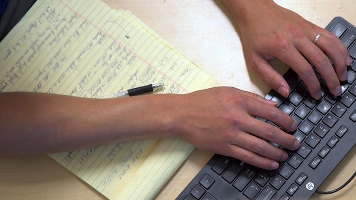 Hands typing on a keyboard next to a notepad